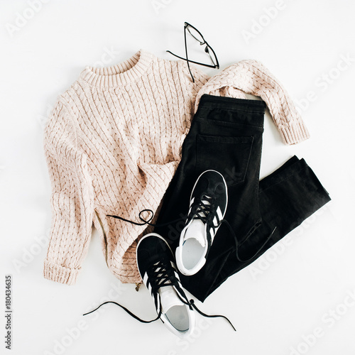 Fashion winter women clothes look on white background. Flat lay, top view. Sweater, sneakers, jeans and glasses.