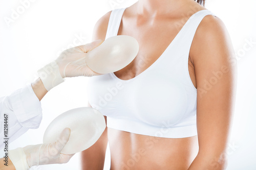 Female doctor choosing mammary prosthesis with her patient over white background.