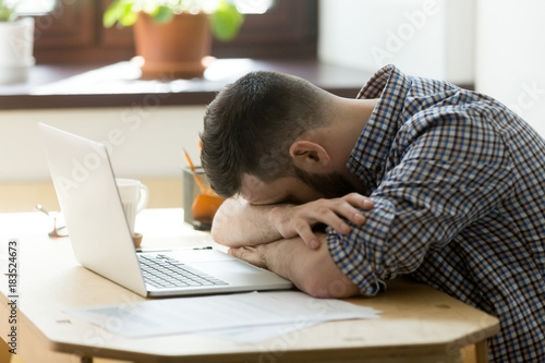 Tired manager falling asleep over laptop in hard working day in home office. Exhausted sleep deprived stressed male worker lying on table and sleeping after overwork, no energy left
