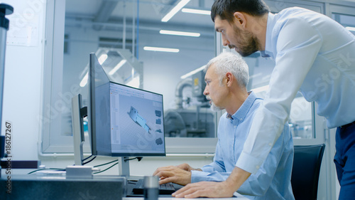 Industrial Designer Has Discussion with Senior Engineer While Working in CAD Program, Designing New Component. He Works on Personal Computer with Two Monitors.