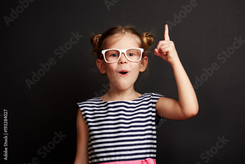 enfant-ayant-une-idee-jolie-fille-dans-des-verres-posant-avec-le-doigt-sur-le-tableau-noir