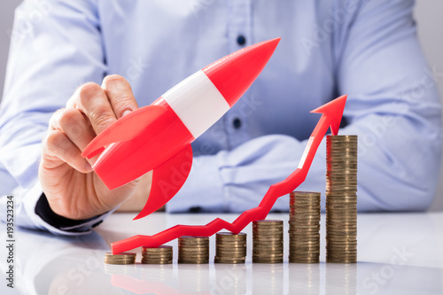 businessperson-flying-rocket-over-increasing-graph-of-coins