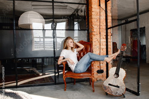 portrait-de-la-jeune-femme-elegante-de-la-blonde-dans-un-t-shirt-blanc-et-un-jean-dans-un-interieur-dans-le-style-du-loft-la-fille-avec-une-guitare