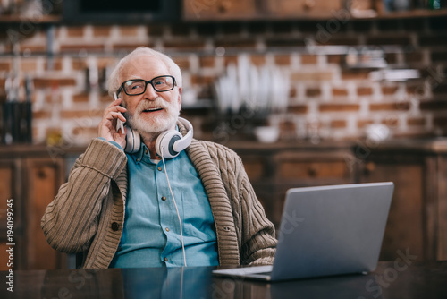 vieil-homme-dans-les-ecouteurs-parler-au-telephone-par-ordinateur-portable