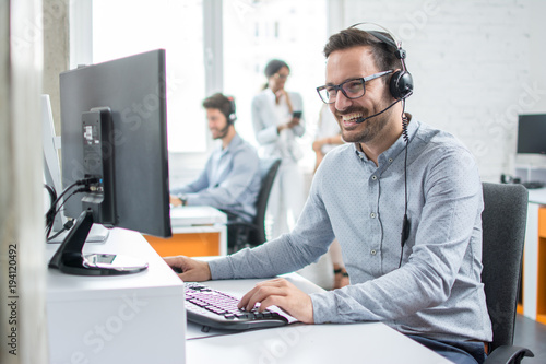 Smiling customer support operator with hands-free headset working in the office. © Bojan