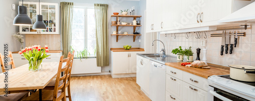 banner of a kitchen with kitchen table and breakfast at the kitchen counter top white cupboards and wooden floor © annaia