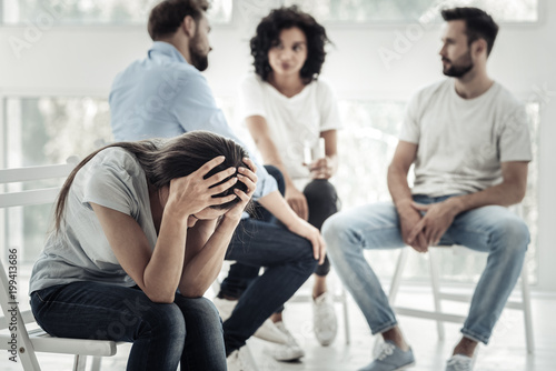 So many problems. Unhappy cheerless pleasant woman sitting on the chair and holding her head while suffering from depression