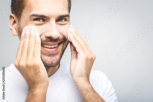 Handsome Man Cleaning Face Skin With Batting Cotton Pads Over Gray Handsome Man Cleaning Face Skin With Batting Cotton Pads Over Gray Background And Looking At Camera