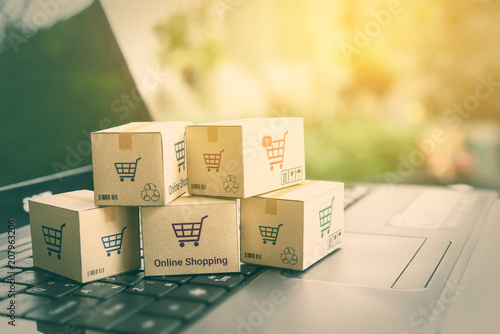 Online shopping / ecommerce and delivery service concept : Paper cartons with a shopping cart or trolley logo on a laptop keyboard, depicts customers order things from retailer sites via the internet. © William W. Potter