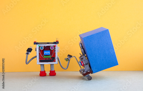 Robotic logistic delivery service concept. Robot moving big blue box container with powered pallet jack. Forklift cart mechanism on gray floor, yellow wall background. Copy space on cardboard box