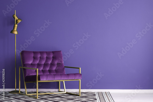Ultra violet armchair with golden details and lamp standing on the empty wall © Photographee.eu