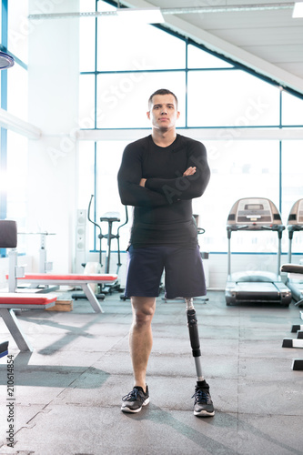 Full length portrait of muscular sportsman with prosthetic leg posing confidently with arms crossed in modern gym, copy space © seventyfour