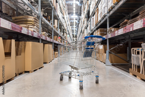 Warehouse storage of retail merchandise shop. Trolley Shopping Cart Between Dry Grocery Shelf Section in Supermarket Warehouse Retail Outlet as Shopping Concept.