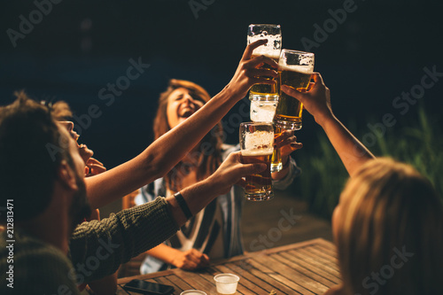 Group of friends drink beer on the terrace and toast during summer night