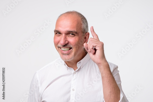 Satisfied mature hispanic man showing index fingers up, giving advice or recommendation