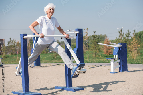 Full length portrait of active senior woman using outdoor exercise machines and enjoying workout, copy space © seventyfour