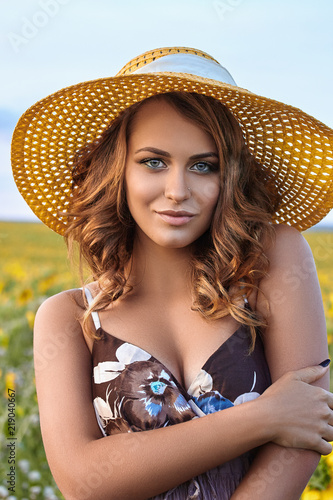 Young beautiful woman wearing a hat in a field of sunflowers © Natali