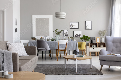 Real photo of a modern living room interior with a dining table and graphics on a wall © Photographee.eu