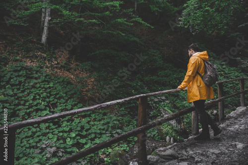 man walking by forest trail to waterfall in yellow raincoat © phpetrunina14