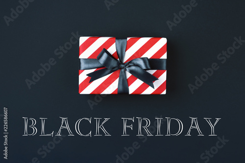 Gift box wrapped in red striped paper and tied with black bow on black background. Black friday concept, top view.