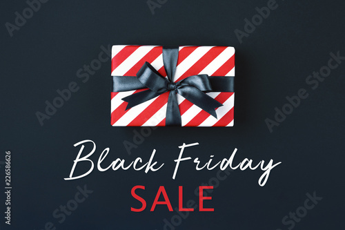 Gift box wrapped in red striped paper and tied with black bow on black background. Black friday concept, top view.