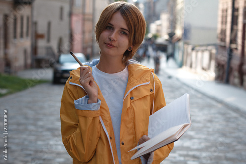 Nice young girl in yellow raincoat holding pen and copybook. Creating poems while walking. © Svyatoslav Lypynskyy