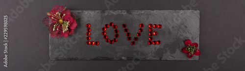 LOVE written with Red Gemstone on Stone with Red flowers background © AnnJane