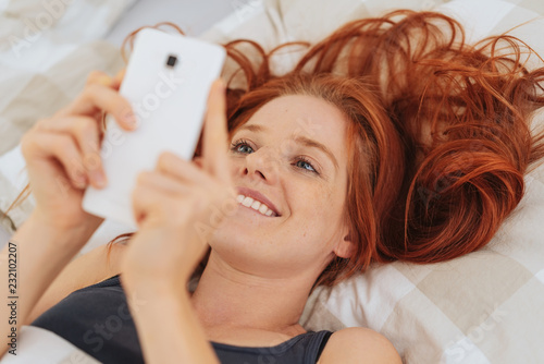 Young smiling woman using mobile phone in bed © contrastwerkstatt