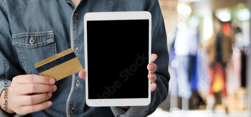 Hand holding credit card and digital tablet with blank on screen for shopping online over blur store background, template, mock up, business and technology concept, online payment, digital money © mangpor2004