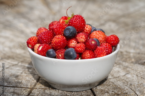 Fresh strawberries and blueberries in a porcelain bowl on a wooden stump © koromelena