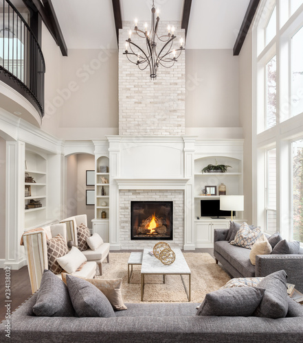 Beautiful Living Room in New Luxury Home with Fireplace and Roaring Fire. Large Bank of Windows Hints at Exterior View. Vertical Orientation © bmak