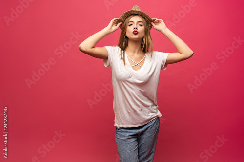 Studio portrait of cheerful female model holding summer hat and smiling. Blonde girl in sunglasses and white shirt having fun during photoshoot © opolja