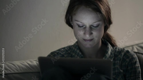 A happy young woman browses the Internet on a tablet computer. Shot in a room with dim lighting, late in the evening. © ptnphotof