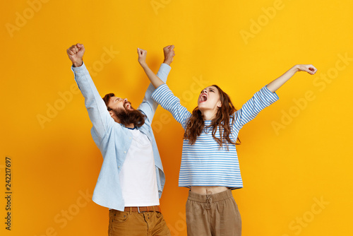 young happy couple won emotionally celebrating win on colored yellow background © JenkoAtaman