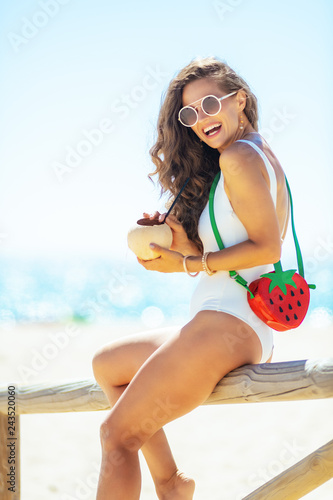 woman sitting on wooden fence with coconut on ocean shore © Alliance