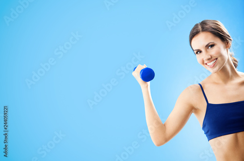 Woman in fitness wear with dumbbell, over blue © vgstudio