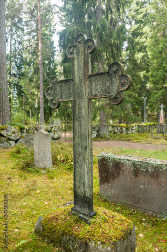 Cross at old semetery in Finland with grave crosses and stones.