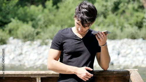 Young handsome man standing in park in summer, using a cell phone to listen to recorded voice message or audio © starsstudio