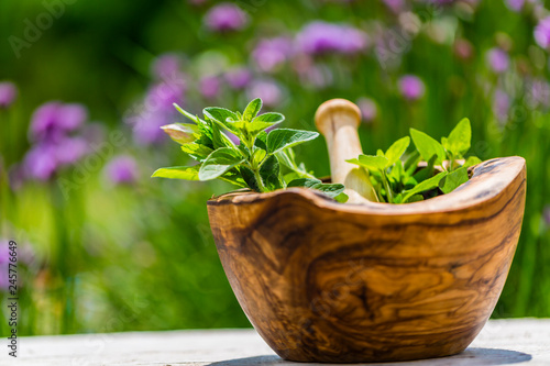 Fresh herbs from the garden in wooden olive mortar against with sunny garden background. Image © Gorilla