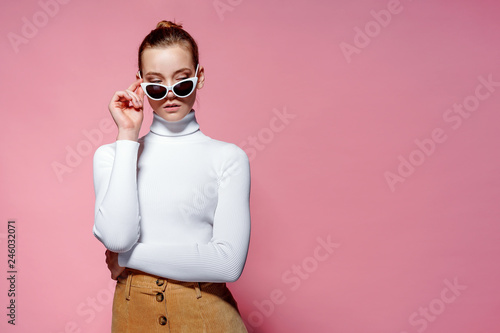 Fashion studio image of gorgeous elegant woman in white knitted golf and sunglasses posing over pink wall. © zamuruev