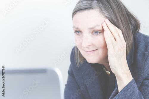 Eine Frau sitzt am Laptop, liest Mails und hält sich den Kopf, da sie Kopfschmerzen hat. © magicpitzy