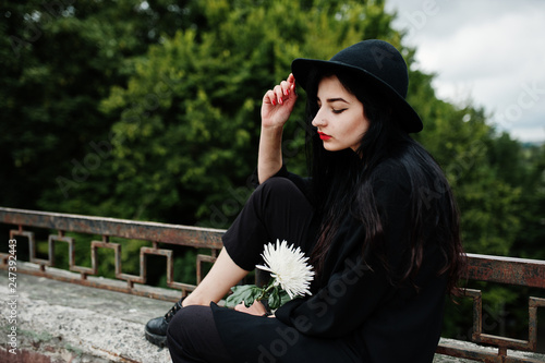 Sensual girl all in black, red lips and hat. Goth dramatic woman hold white chrysanthemum flower. © AS Photo Project