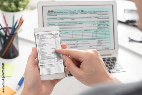 Man filling tax information using mobile devices © Proxima Studio