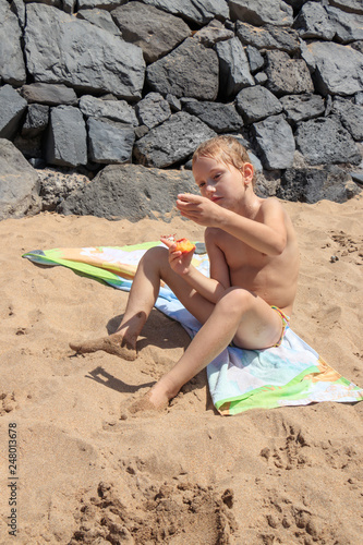 a child eats a peach on a sandy beach after swimming in the ocean © Uladzimir