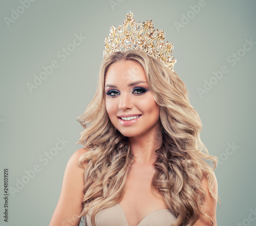 Attractive blonde woman fashion model with long curly hair, makeup and gold crown on background with copy space © millaf
