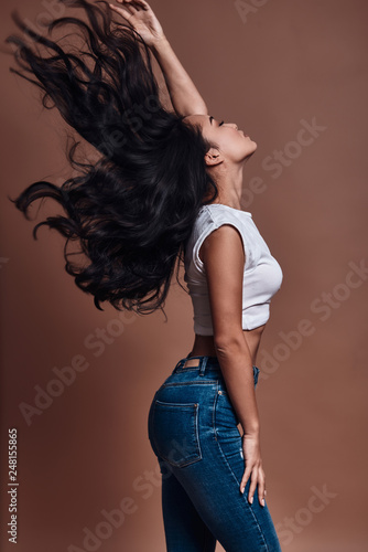 Strong hair. Beautiful young woman touching her hair while standing against brown background © gstockstudio
