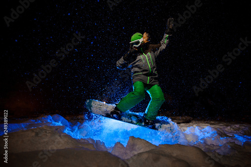 Female snowboarder dressed in a green sportswear jumping on the mountain slope © fesenko