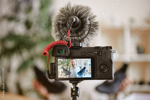 In focus. Close up photo of camera display with cheerful male blogger holding black sneakers while recording new video