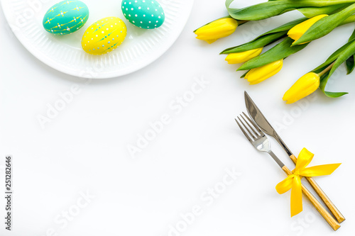 Festive Easter table decorated with tulips. Tableware and painted eggs on white background top view copy space © 9dreamstudio