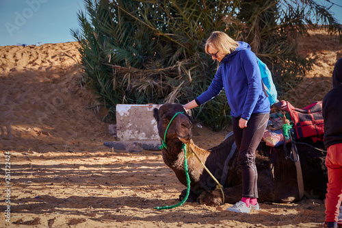 Happy blonde tourist girl petting the camel in the Sahara desert © Lukas